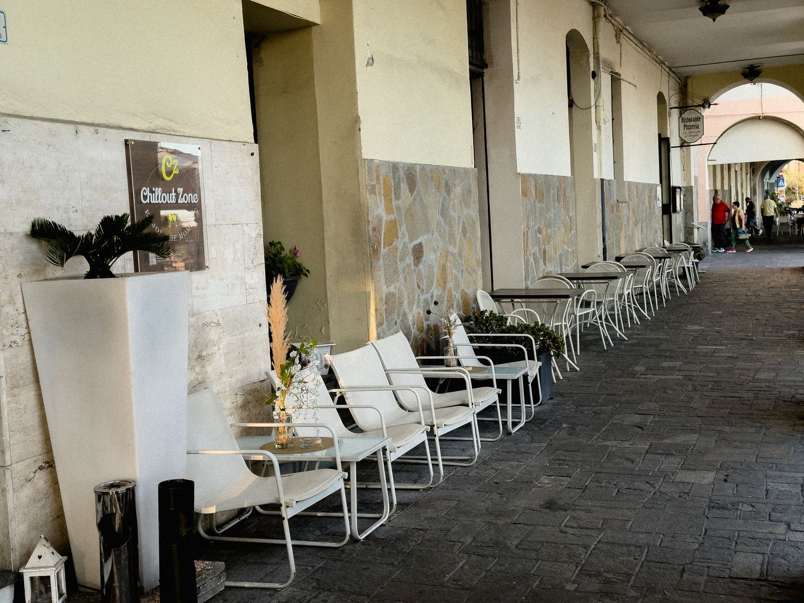 Dehors sotto i portici di Calata Cuneo a Imperia: poltroncine bianche e tavolini del Chillout Zone, aperitivo e cocktail bar