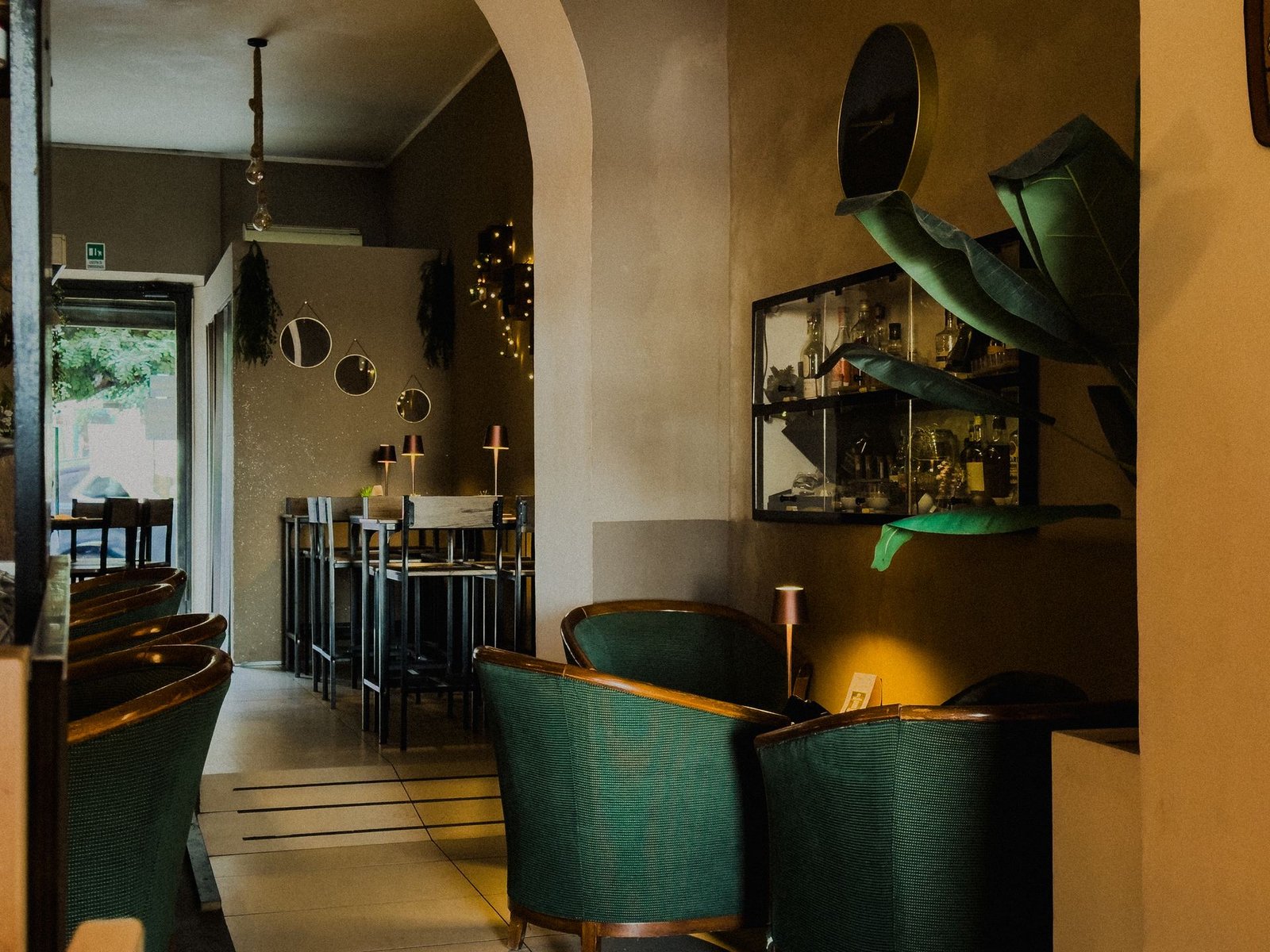 Poltroncine verdi vintage, vetrina con distillati e piante nel Chillout Zone, cocktail bar e lounge a Imperia